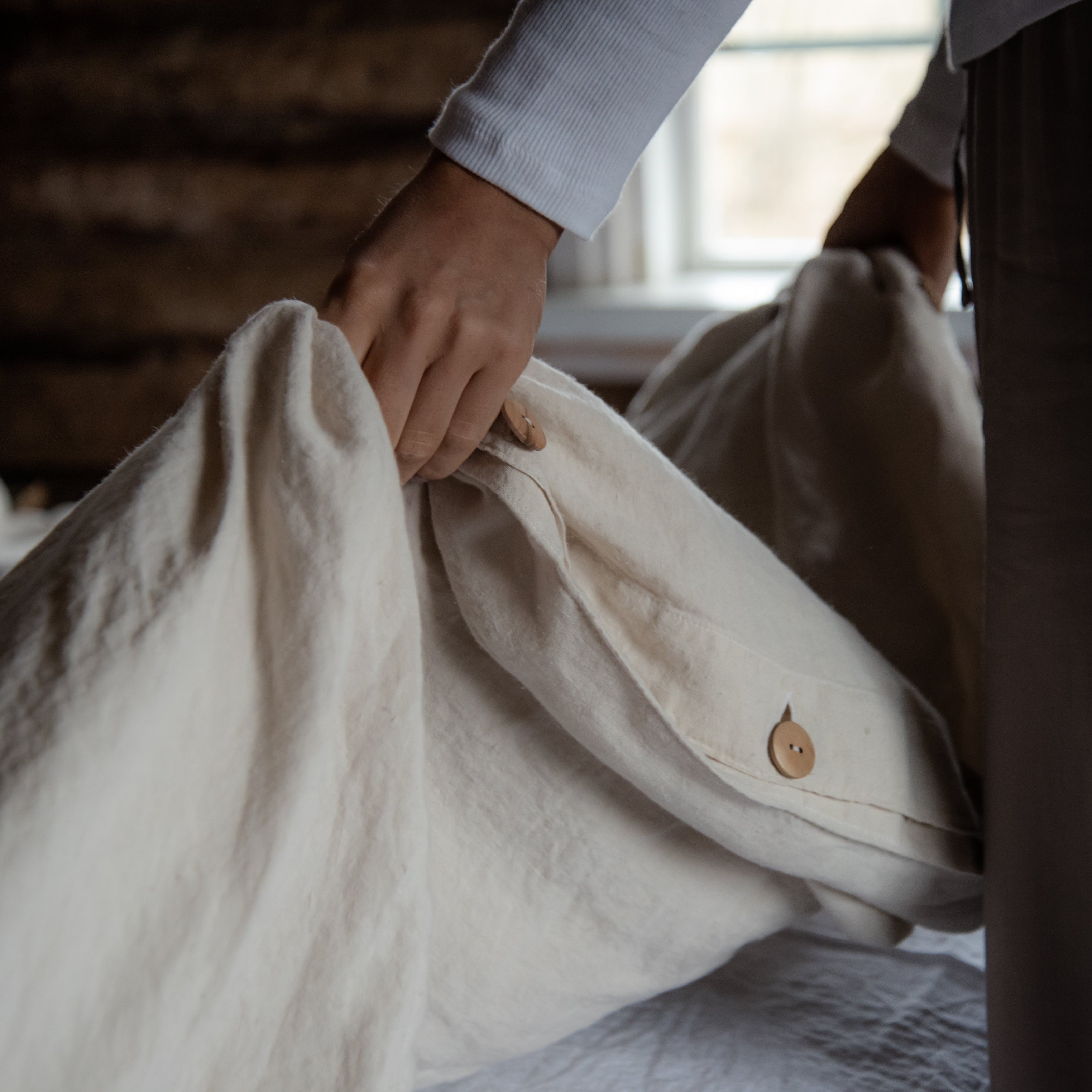 Person adjusting a beige pillow on a bed in a softly lit room.