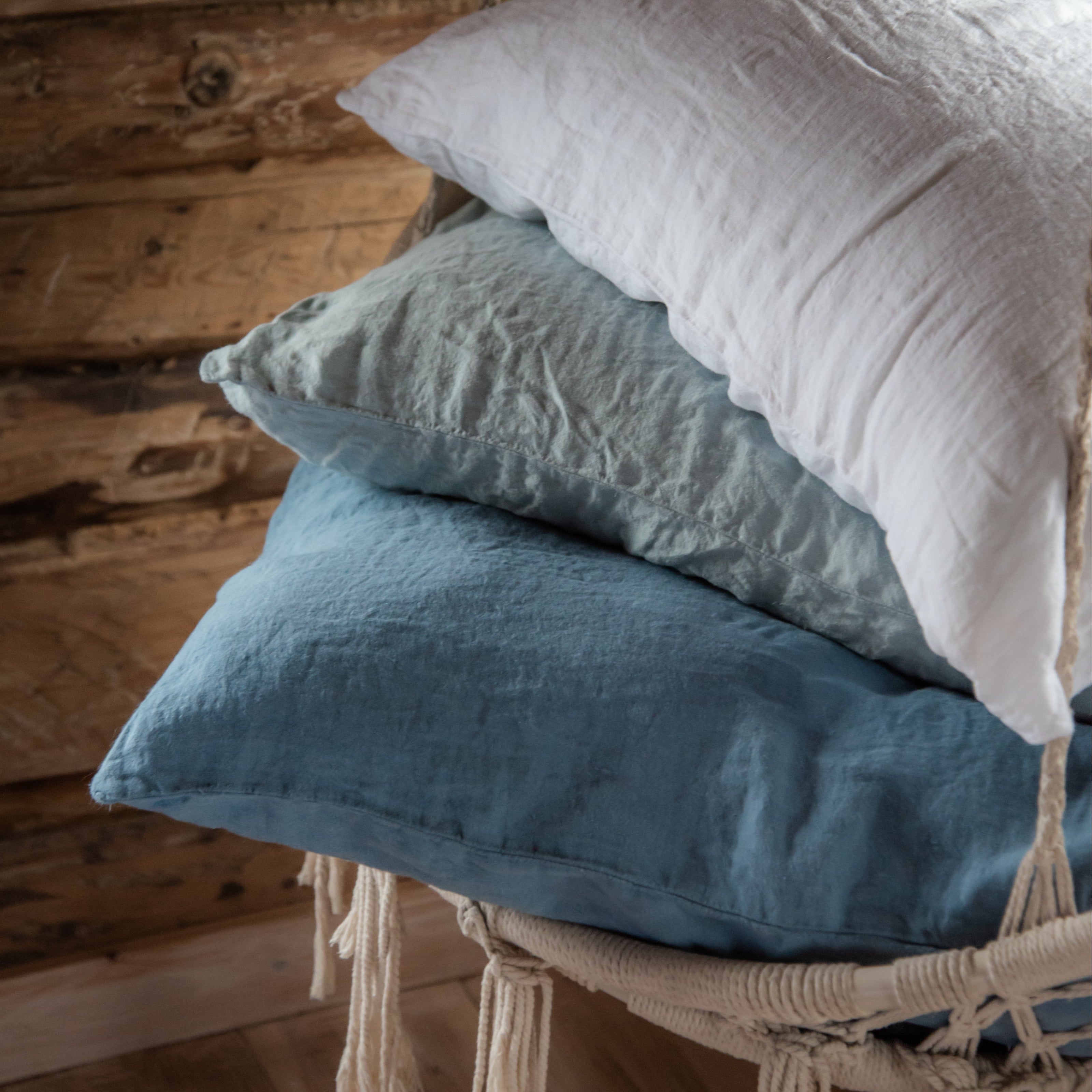 Three pillows in white, blue, and green hanging on a wooden wall.